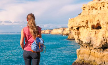 Uçurumun, mağaranın ve rocj oluşumunun güzel manzarasının keyfini çıkaran kadın, Portekiz 'de Algarve