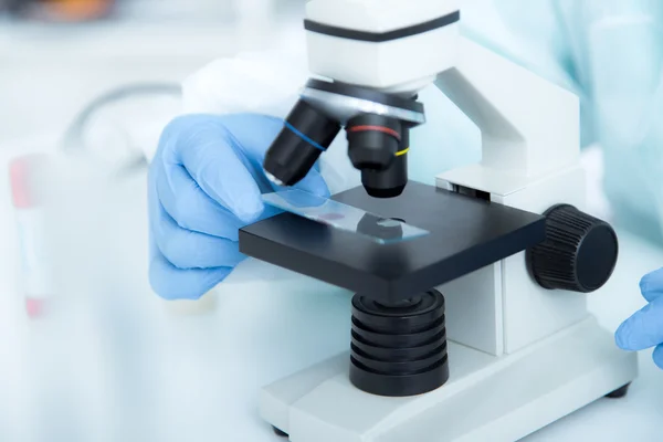 Mujer en un microscopio de laboratorio con la diapositiva del microscopio en la mano . —  Fotos de Stock