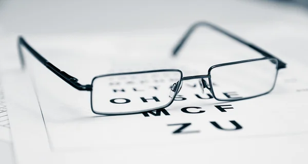 Limpar óculos modernos pretos em uma tabela de teste de visão ocular — Fotografia de Stock