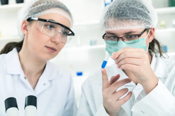 Clínico sério estudando elemento químico em laboratório com seu assistente por perto — Fotografia de Stock