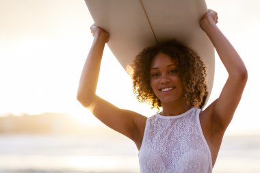 Günbatımında sörf tahtası tutan karışık ırk kadın