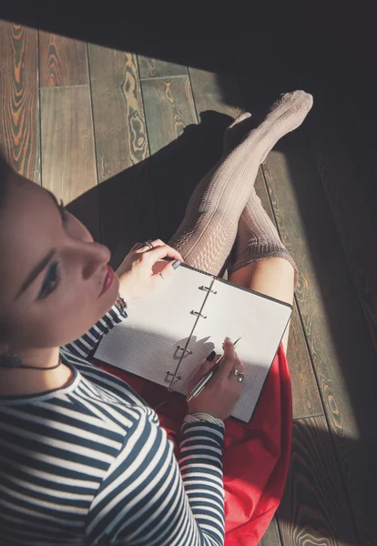 Уютное фото молодой женщины, которая пишет в блокноте, сидя на гриппе — стоковое фото