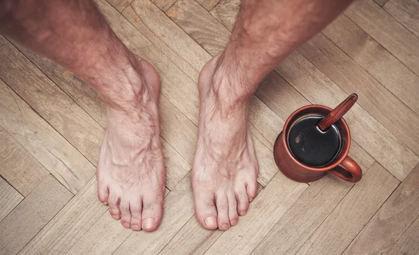 Männerfüße auf dem Boden und eine Tasse Kaffee — Stockfoto