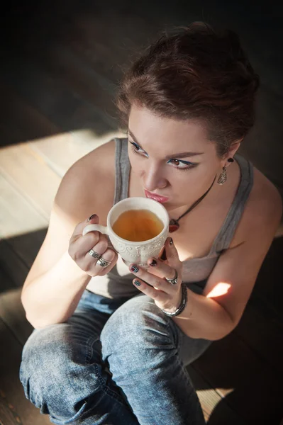 Útulné fotografie mladé ženy s šálkem čaje, sedí na podlaze — Stock fotografie