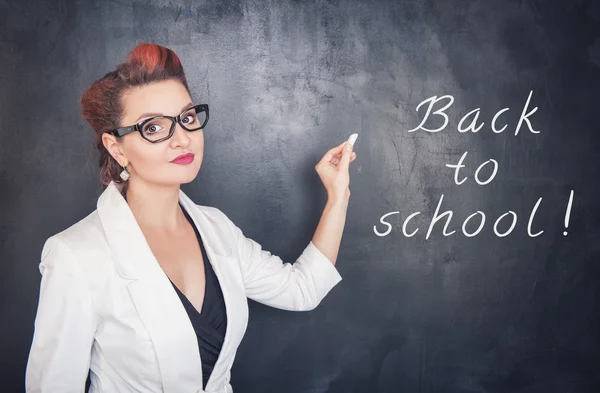 Beautiful teacher with piece of chalk on blackboard background — Stock Photo, Image