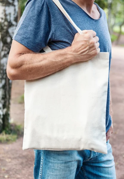 Hombre sosteniendo bolsa de lona vacía. Plantilla maqueta arriba —  Fotos de Stock