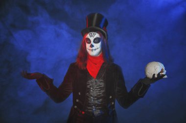 Korkunç Cadılar Bayramı 'na sahip yakışıklı adam ölü Calavera stili makyaj yapıyor. Mavi dumanlı arka grubunda kafatası var.