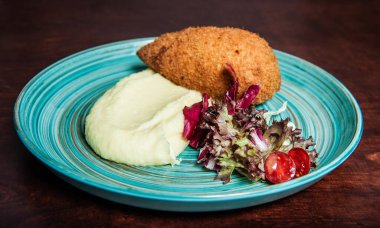 Geleneksel Kiev pirzolası, patates püresi ve tabakta salata.