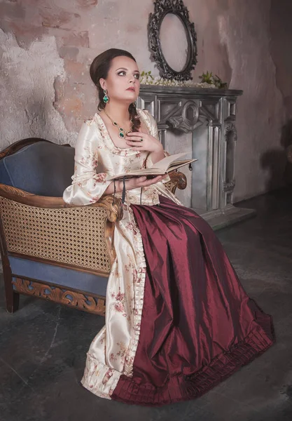 穿着中古时代旧衣服 头戴书本的漂亮女人坐在沙发上 — 图库照片