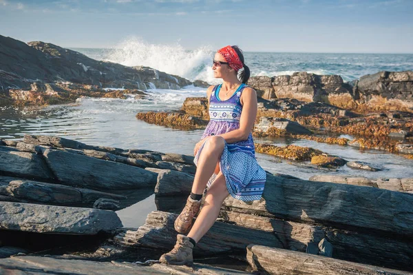 漂亮的女人穿着衣服坐在岩石上的大石头上抵御海浪 — 图库照片