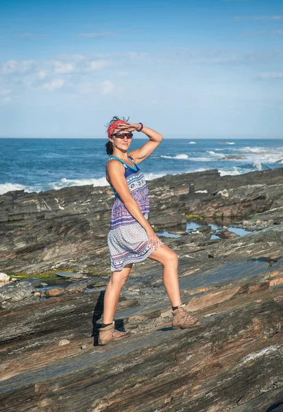 美丽的女人穿着衣服站在岩石的大石头上抵御海浪 — 图库照片