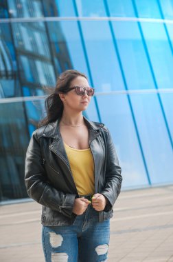 Saçları rüzgarda savrulan güzel, genç bir kadın şehrin arka planındaki ayna duvarında.