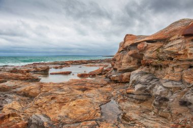 Büyük kızıl kaya ve deniz dalgaları dramatik mavi gökyüzü arka planına karşı