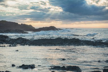 Büyük kayalar, deniz, güneş ışığı ve güzel gün batımıyla dramatik bir sahne.