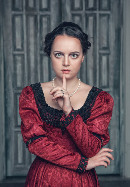 Beautiful medieval woman in red dress making silence gesture