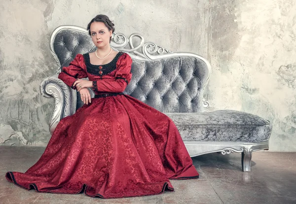 Mulher bonita em vestido medieval vermelho no sofá — Fotografia de Stock