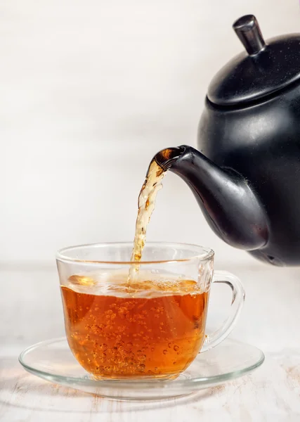 Xícara de chá com chá derramando e bule preto — Fotografia de Stock