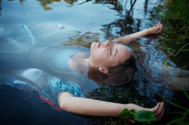Young beautiful drowned woman in blue dress lying in the river clipart
