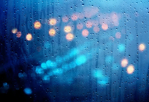 Drops of rain on glass with defocused lights. Urban abstract bac — Stock Photo, Image