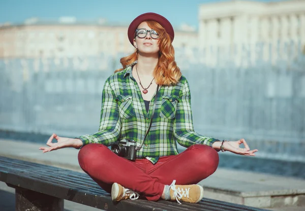 Csípő vöröshajú nő kalapot és szemüveg jóga a padon — Stock Fotó