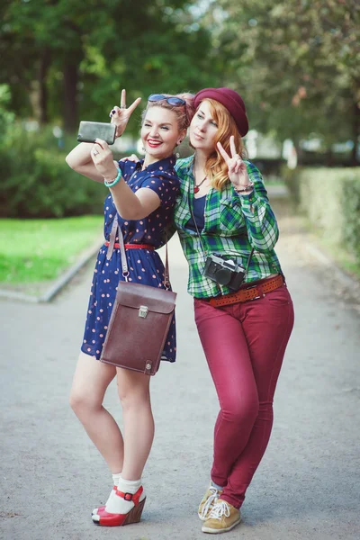 Deux filles hipster avec bretelles prenant des photos d'elles-mêmes sur m — Photo