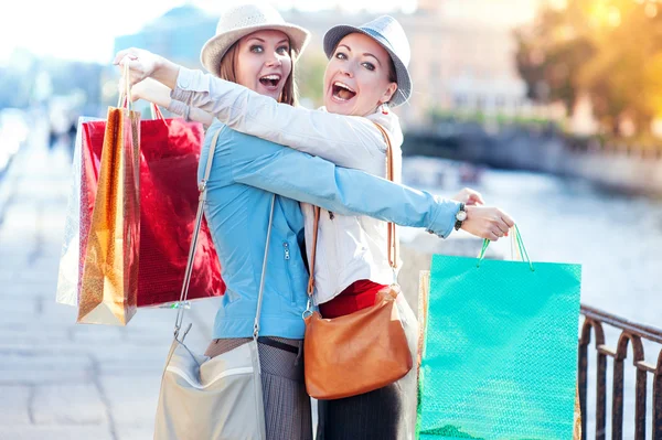 Twee gelukkige mooie meisjes met boodschappentassen omarmen in de stad — Stockfoto