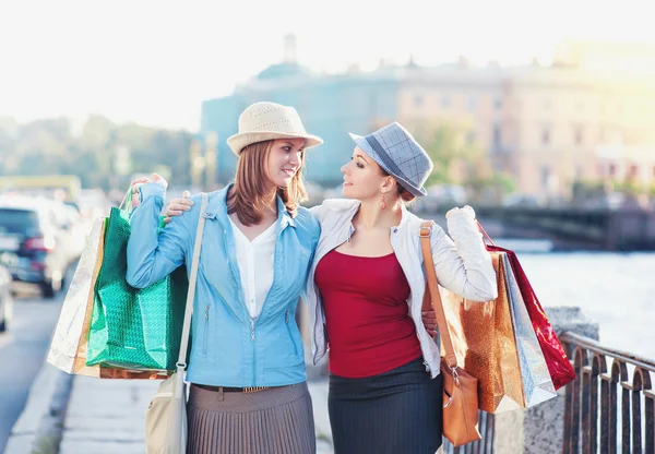 Två glada vackra flickor med shoppingkassar omfamna i staden — Stockfoto