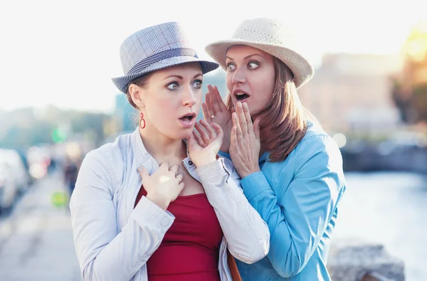 Junge schöne Frau, die ihrem Freund in der Stadt ein Geheimnis erzählt — Stockfoto