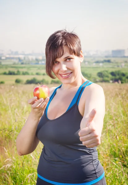Fitness beautiful plus size woman with apple showing thumbs up — Stock Photo, Image