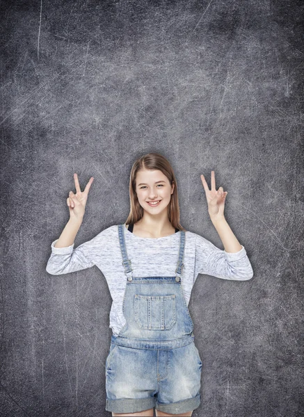 Happy teenager girl showing victory sign on the chalkboard backg