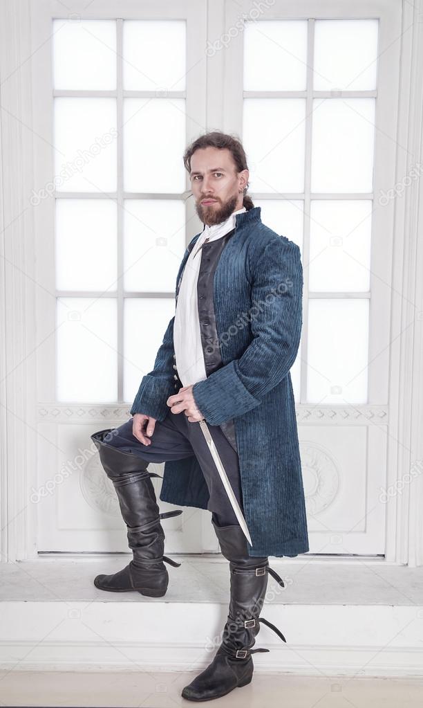 Young handsome man in medieval clothes with sword standing