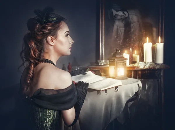 Жінка з книгою в ретро сукні і привидом у дзеркалі — стокове фото