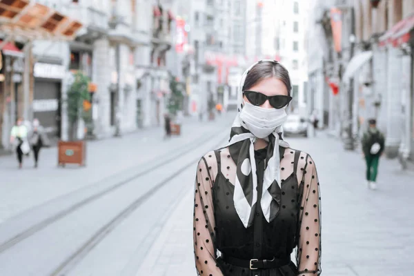 Attraktiv ung kvinna i halsduk på huvudet och en medicinsk mask på gatan i en europeisk stad. Lady promenader på offentlig plats bär prtotective mask — Stockfoto