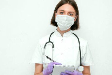 Young woman doctor with stethoscope in white coat, gloves and medical mask holding note.