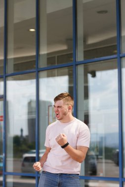 Başarımızı kutlamak için tişört giyen neşeli, heyecanlı adam. Yumruklarını sıkmaya devam et. İyi şansla mutlu. Adam evet diyor..