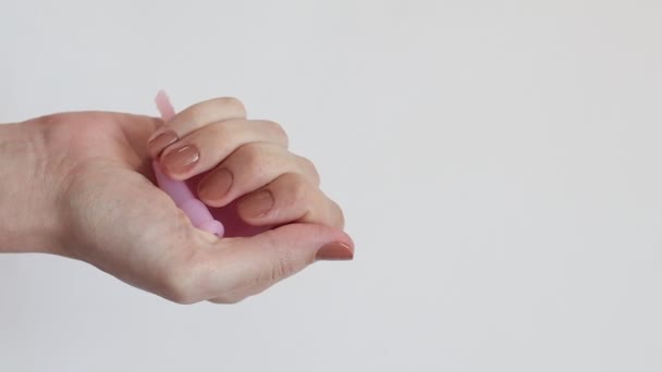 Mladá žena ruka drží opakovaně použitelný růžový silikonový menstruační pohár na bílém pozadí — Stock video