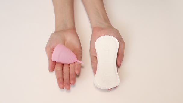 Junge Frauenhände halten Damenbinden und wiederverwendbare rosa Silikon-Menstruationstasse — Stockvideo