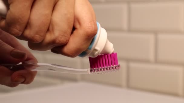 Feche apertando pasta de dentes branca na escova de dentes rosa. Produtos de higiene pessoal. Rotina diária da manhã — Vídeo de Stock