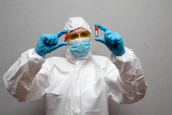 Woman doctor in protective suit and mask holding coronavirus infected blood sample test tube.