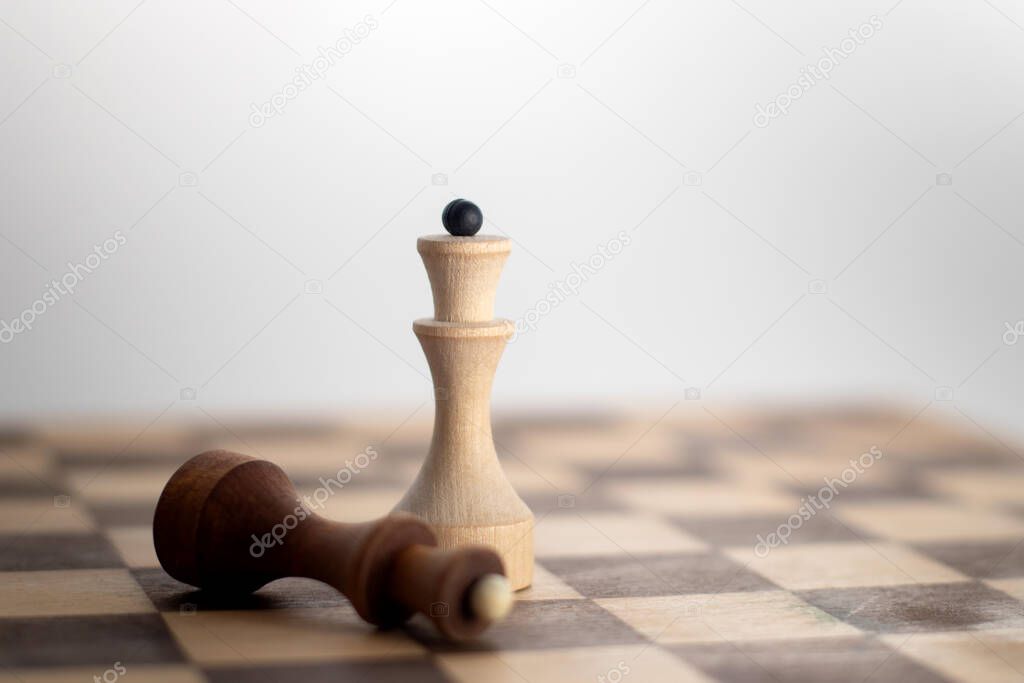 White queen chess surrounded by a fallen silver black chess piece on chess board game.