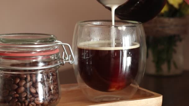 Выливать молоко в стакан черного кофе. Сливки наливают в стакан кофе. — стоковое видео