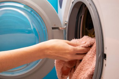 Ev hanımı çamaşır makinesine çamaşır koyuyor. Çamaşırları çamaşır makinesine yüklemek için eller..