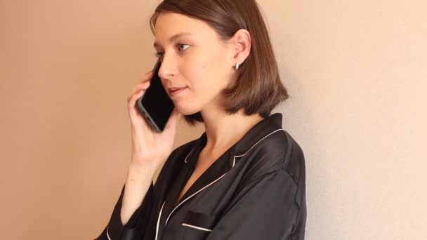 Mujer joven en pijama negro hablando por teléfono en la mañana — Vídeo de stock