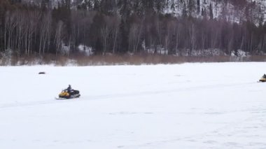 Donmuş nehirde kar motosikletine binmek. Kar motosikleti sürücüsü donmuş nehirde ilerliyor. Aşırı kış aktiviteleri. Adam kar kamyonundan kurtuldu.