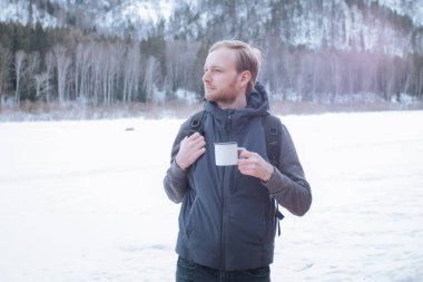 Sırt çantalı bir adam dağların arka planında bardak tutuyor..