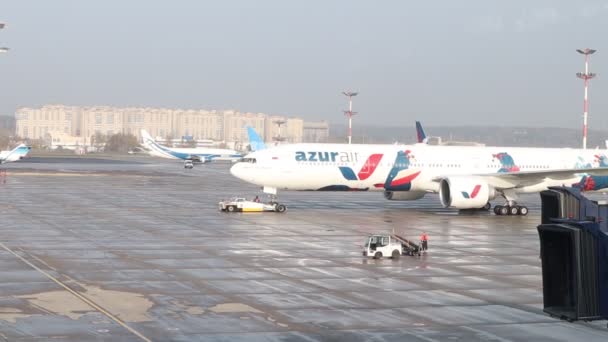 L'aereo è trainato lungo la pista. Preparazione pre-volo di un aereo della compagnia aerea Azur Air all'aeroporto internazionale di Vnukovo. Veicoli di servizio che caricano bagagli sull'aereo — Video Stock
