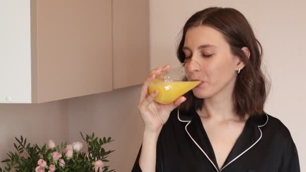 Giovane donna che beve succo d'arancia in cucina a casa — Video Stock