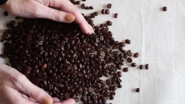 Mano mostrando granos de café. Granos de café tostados frescos en una superficie de trapo bolsa — Vídeos de Stock