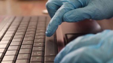 Mavi tıbbi eldivenlerle klavyeyi kullanmak. Klavyeye yazı yazan eller.