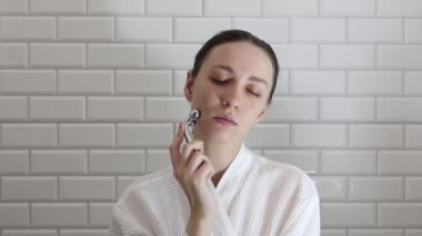 Yaşlı karşıtı masaj için yüz silindiri kullanan bir kadın. Metal bir masajcıyla yüz masajı yapan genç bir kadın.